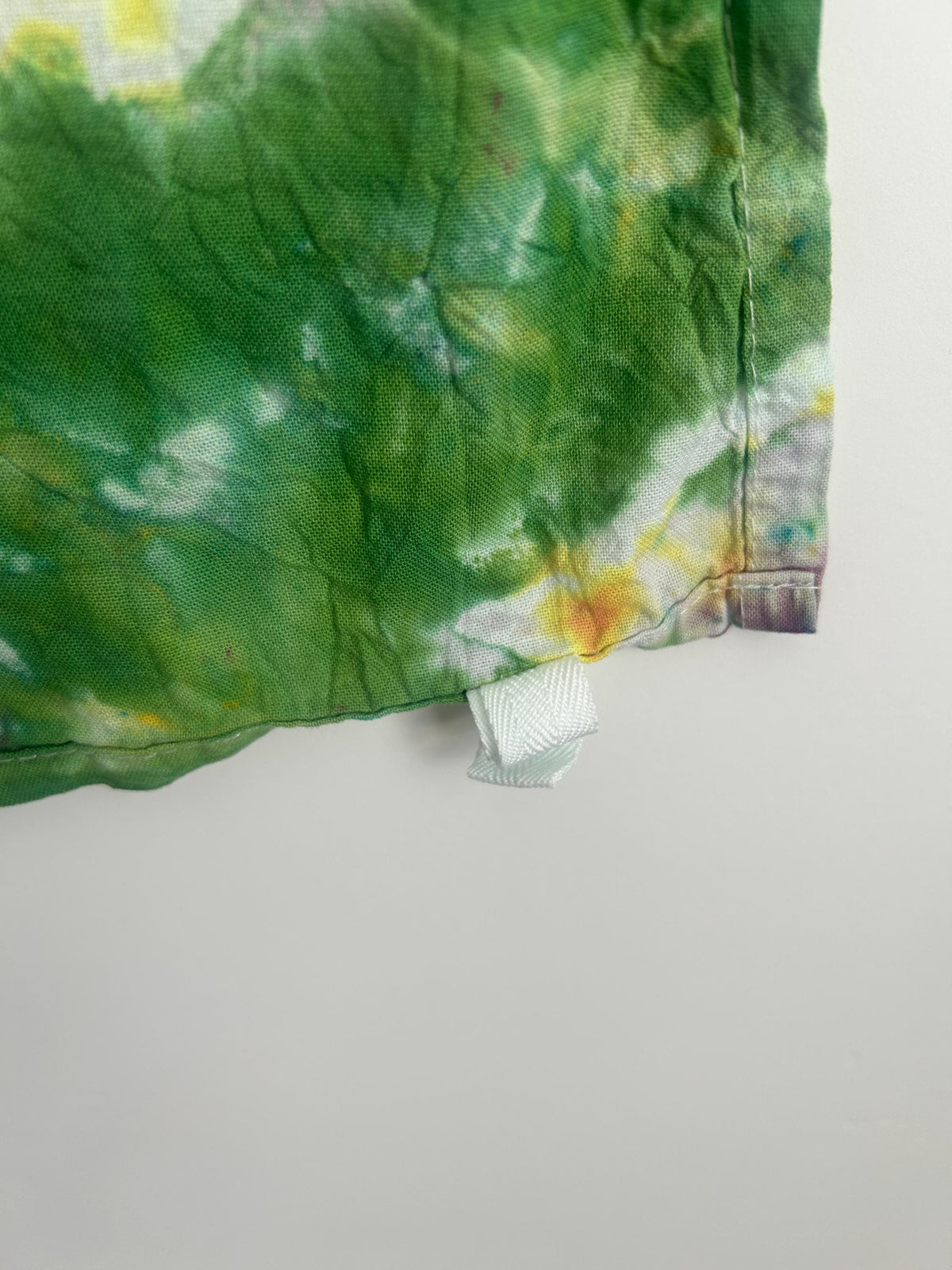 Corner detail of hand dyed cotton tea towel showing fabric texture and care label