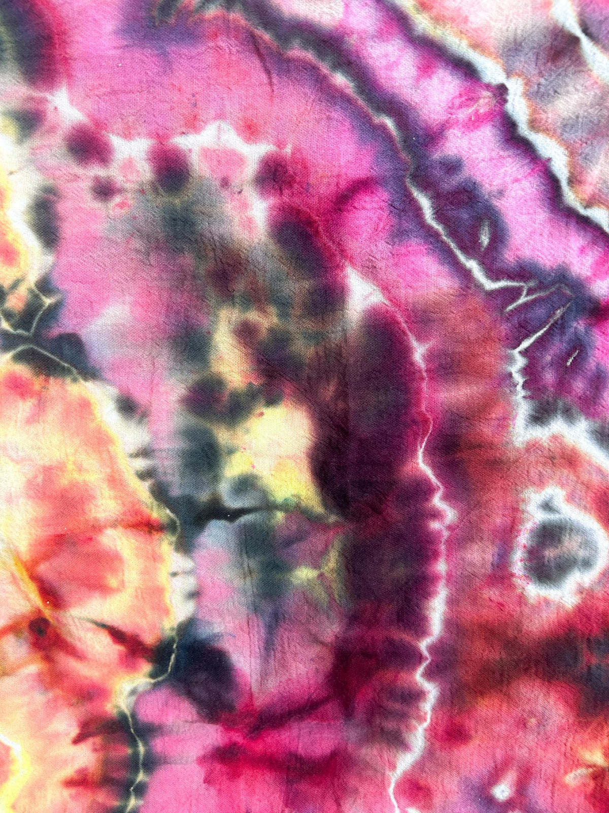 Close-up of a bold ice dye tea towel showing magenta, fuchsia, purple, and gold geode patterns.