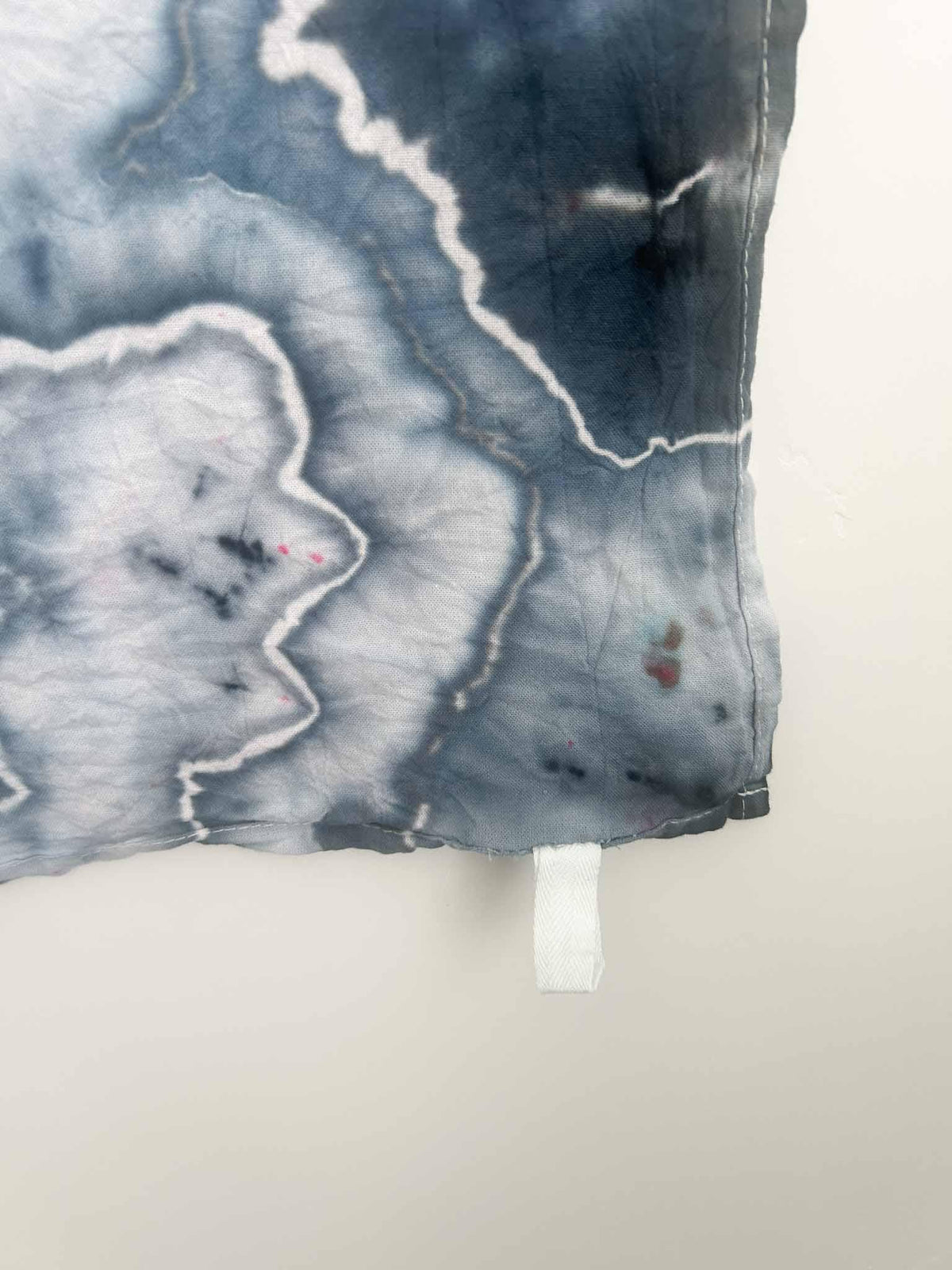 Corner detail of slate blue ice dyed tea towel showing hem stitching and white hang loop