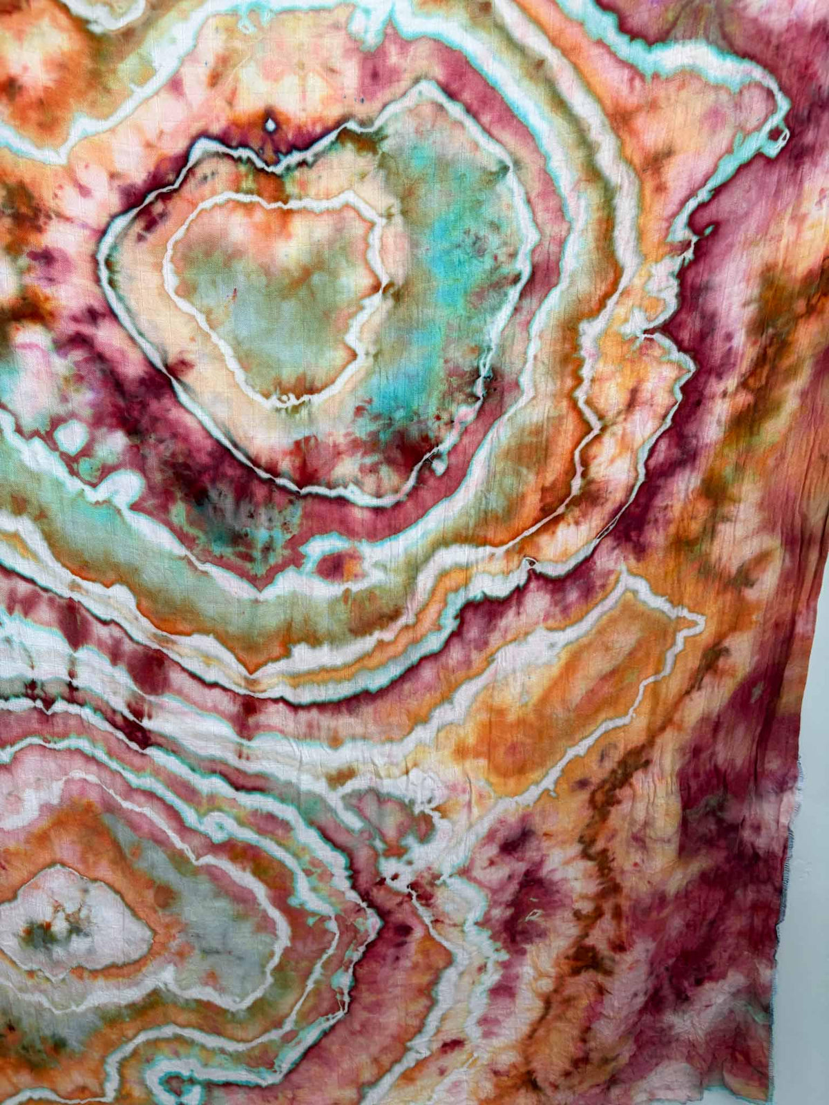 Close-up of an ice dyed geode with white lines edged in turquoise, circling a center of sage green and aqua surrounded by raspberry and orange rings. __etsy:8672499389