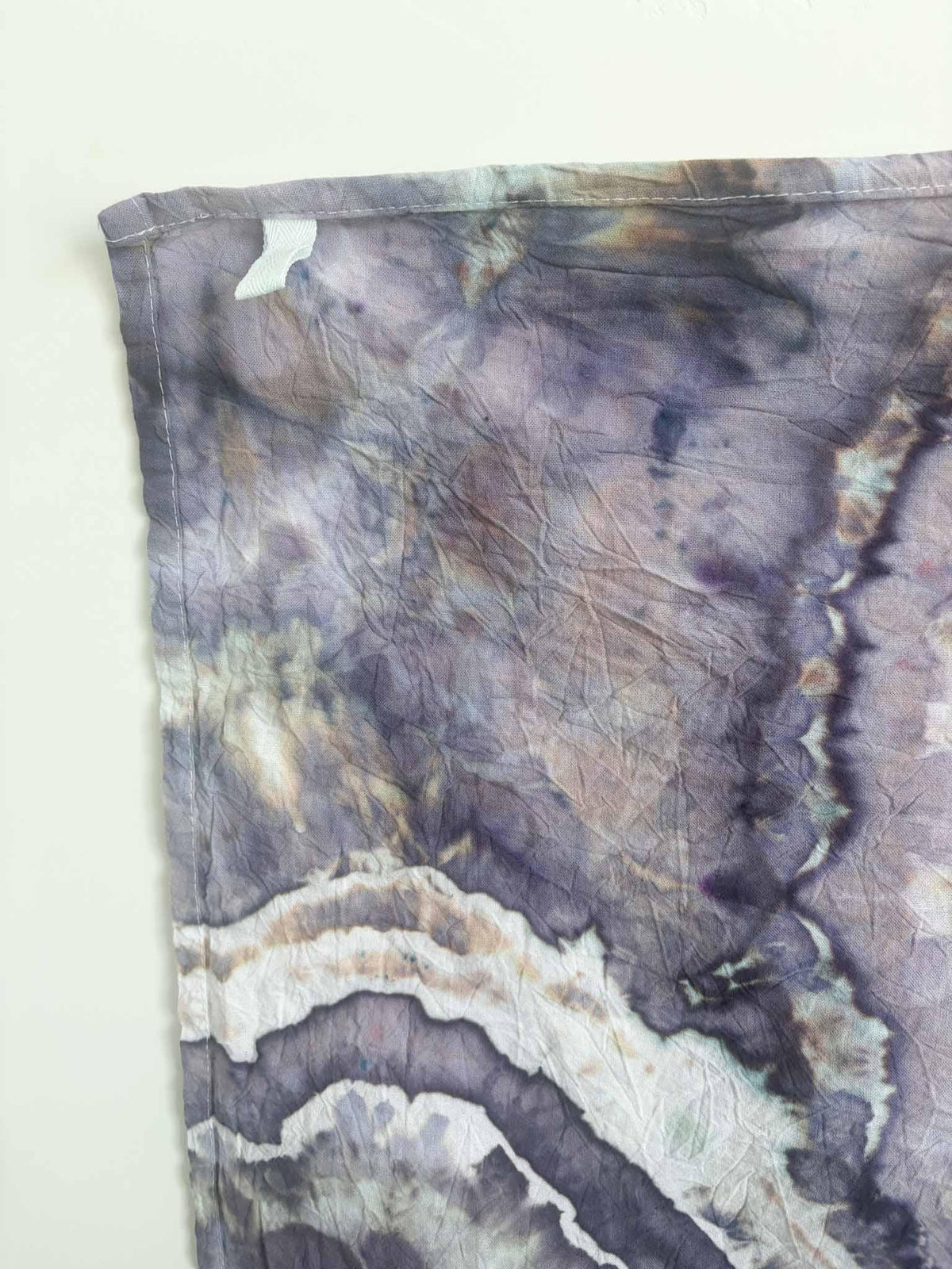 Corner of a lavender and slate purple ice dyed tea towel with a pale twill hanging loop stitched into the hemmed edge. __etsy:8624616376