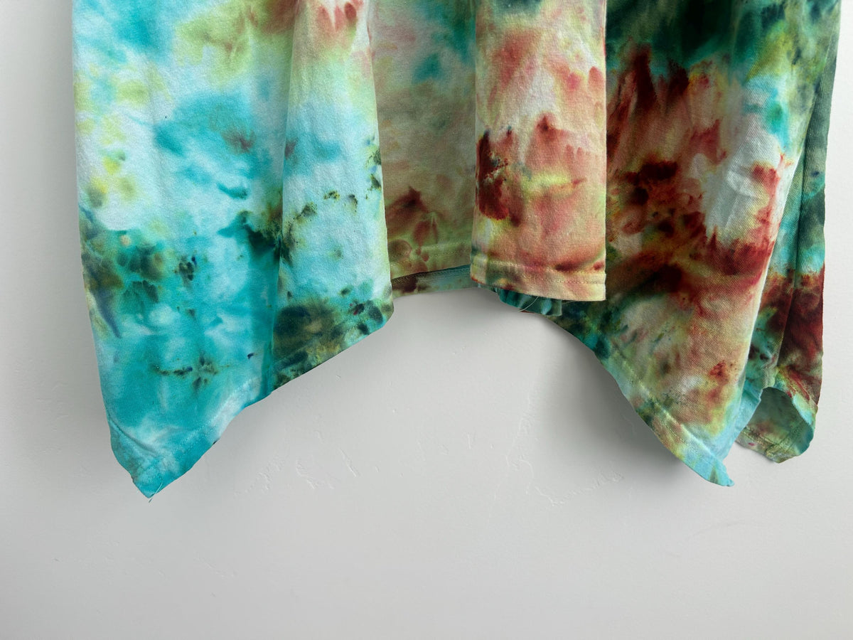 Bottom hem of hand dyed cotton dress featuring flowing purple, teal, and mint ice dye pattern and asymmetrical drape
