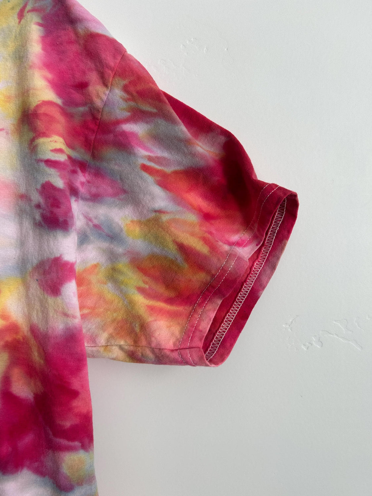 Sleeve and hem detail of a hand-dyed raspberry pink ice dye cotton t-shirt showing vibrant color saturation and artisan dye technique, size L.