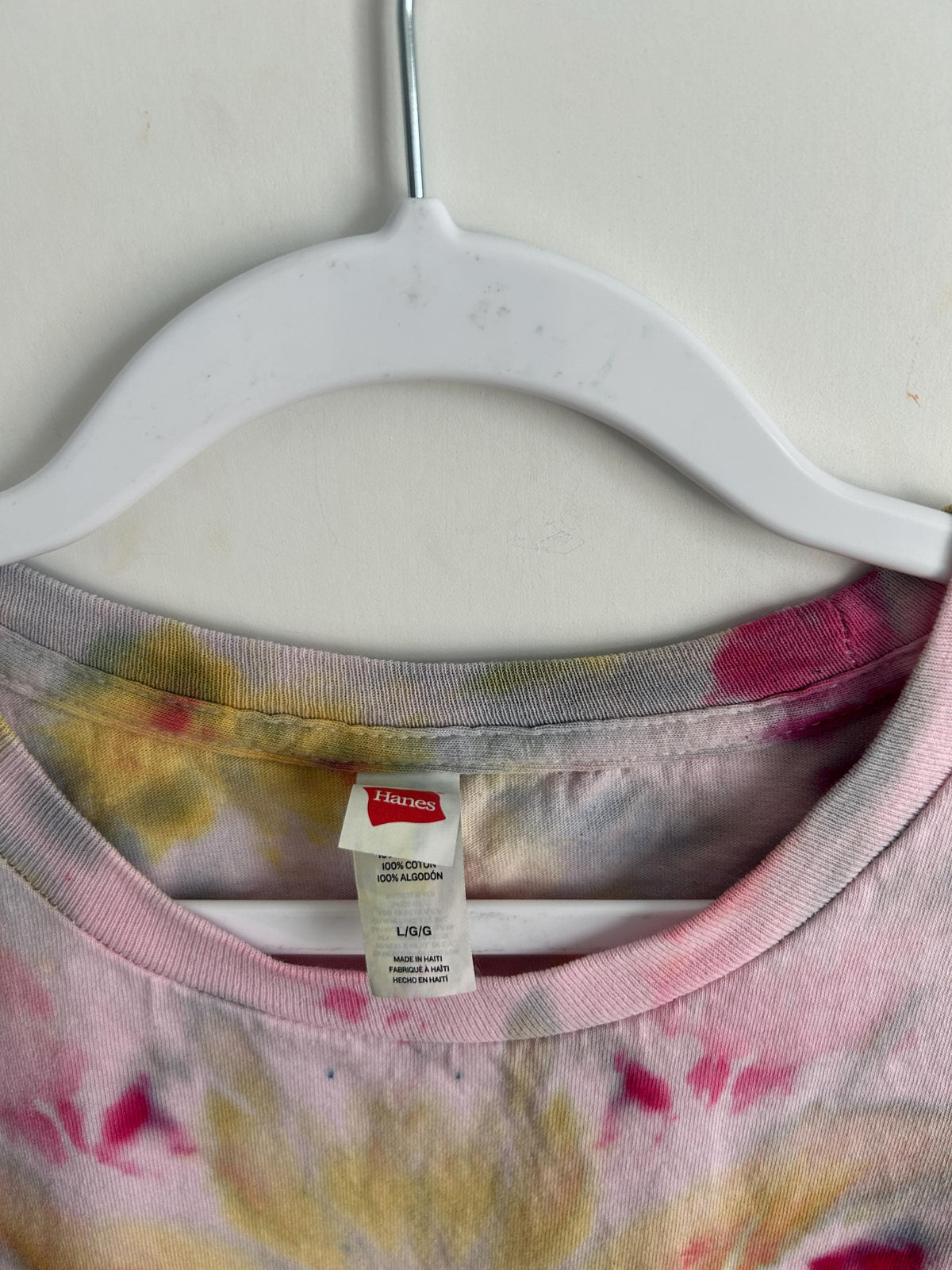 Close-up of Hanes size L neckline on a hand-dyed raspberry and yellow ice dye t-shirt, showing soft pink collar dye and artisan craftsmanship.