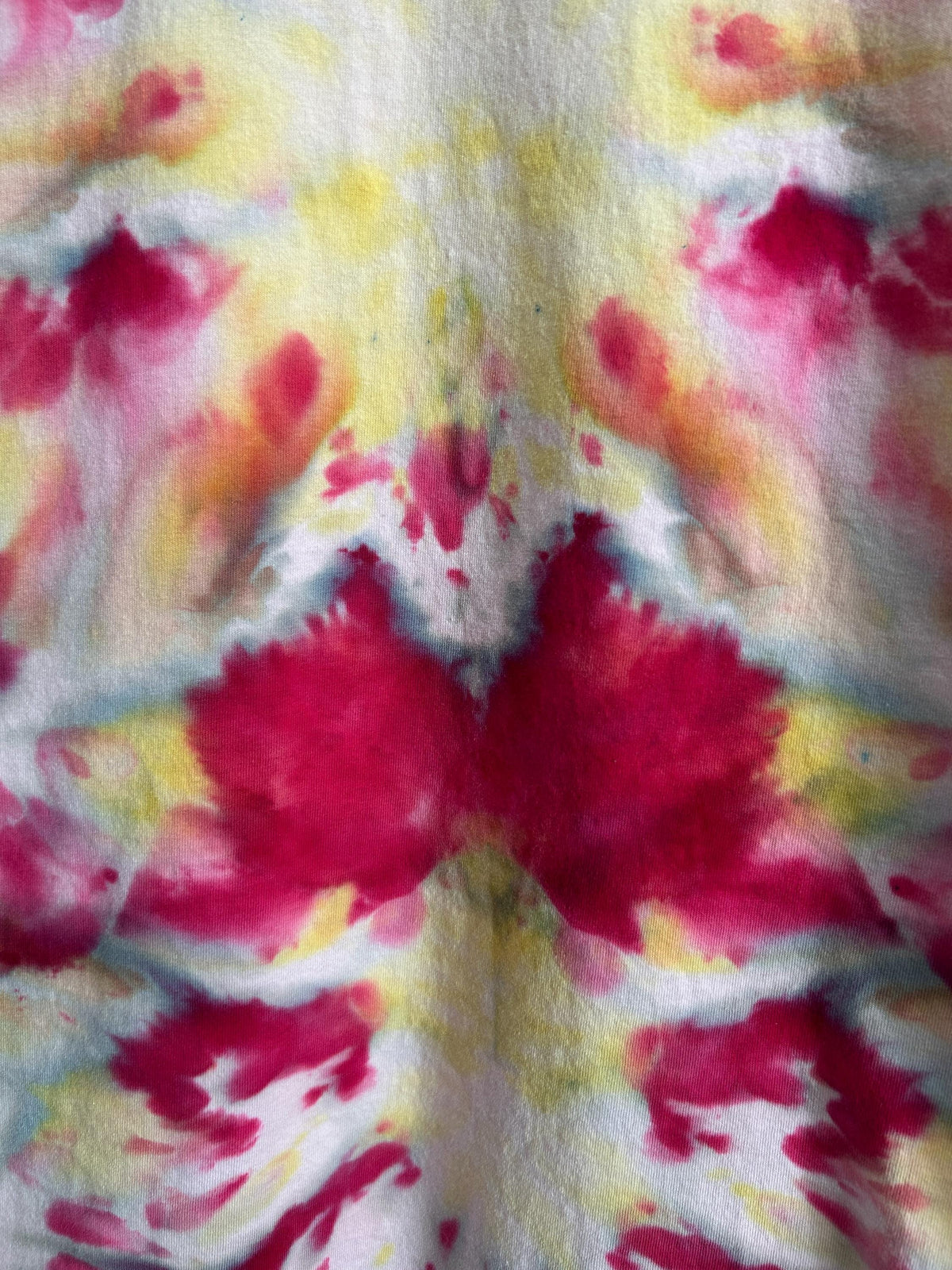 Macro detail of a flat fold ice dye pattern showing raspberry and yellow blooms on white cotton. Artisan fiber-reactive dye with mirrored symmetrical design.