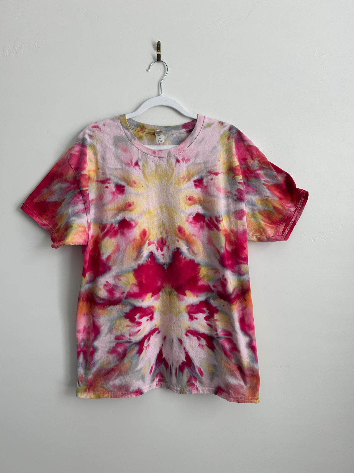 Hand-dyed ice dye t-shirt in raspberry pink, golden yellow, and soft grey. Mirrored kaleidoscope pattern on 100% cotton, one-of-a-kind artisan tie dye tee, size L.