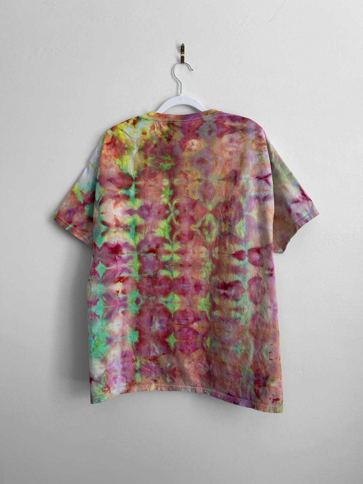 Back of ice dye t-shirt in XL on white hanger showing symmetrical kaleidoscope tie dye pattern in pink, green, coral, and magenta on light background
