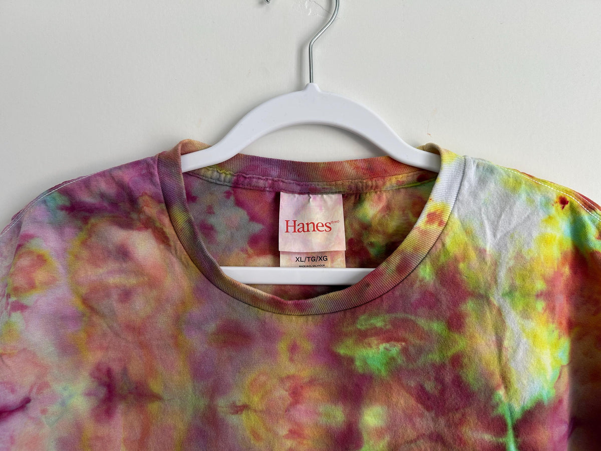 Upper front of ice dye t-shirt showing neckline and Hanes XL label, watercolor-style tie dye pattern in pink, green, yellow, and teal
