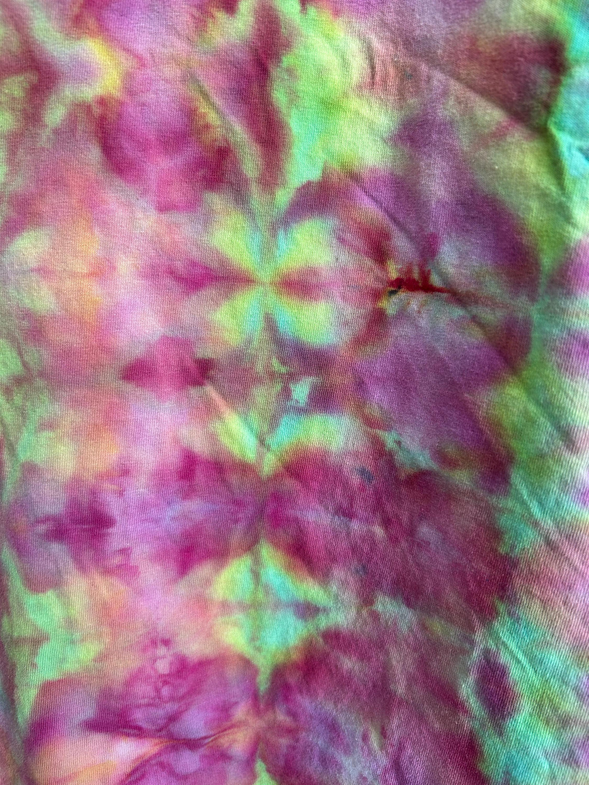 Close-up detail of ice dye pattern on cotton t-shirt showing magenta, lime green, mint, and coral kaleidoscope design created with fiber reactive dye