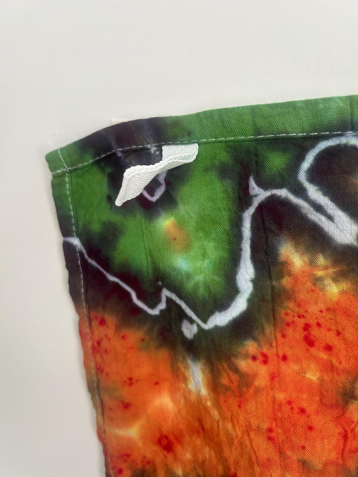 Corner detail of hand dyed cotton tea towel showing hemmed edge and care label