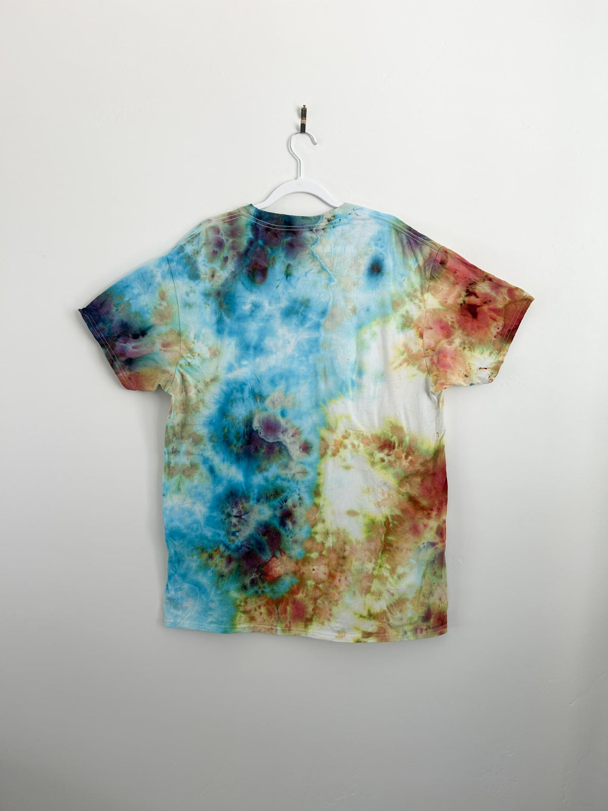 Back view of multicolor ice dye tee showing teal blue, deep purple, warm rust, and soft yellow in a painterly scrunch pattern