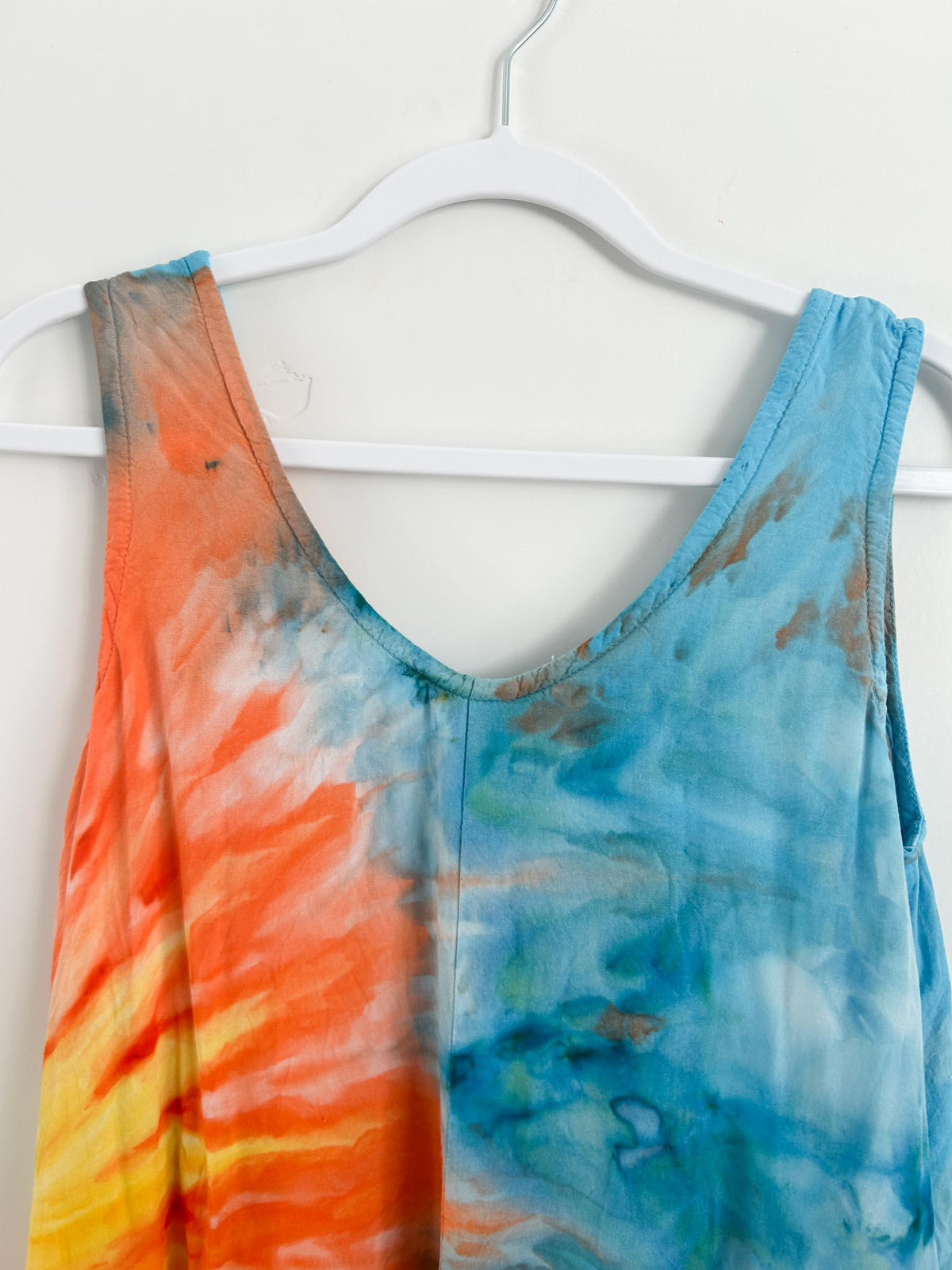 Sleeveless V neck and shoulder straps of tie dye sundress showing orange sunburst meeting blue watercolor