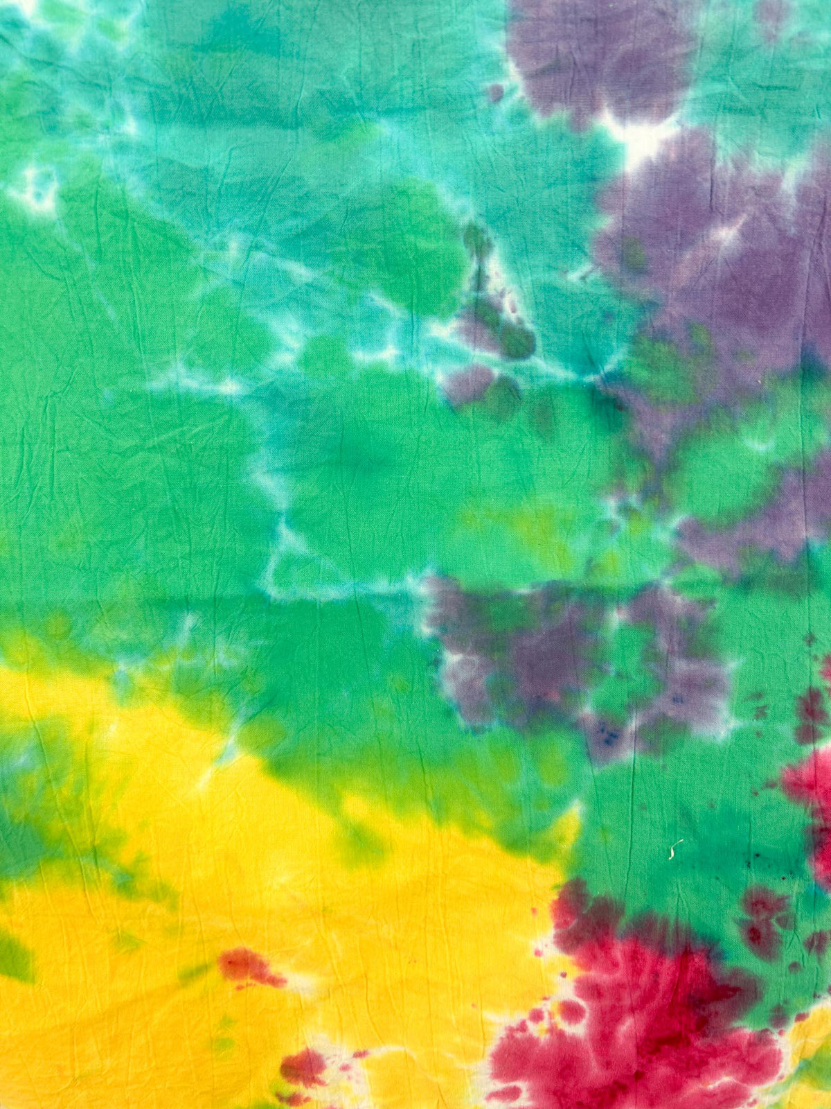 Close up of rainbow tie dye pattern on cotton flour sack towel showing yellow, green, teal, magenta, and purple watercolor blends