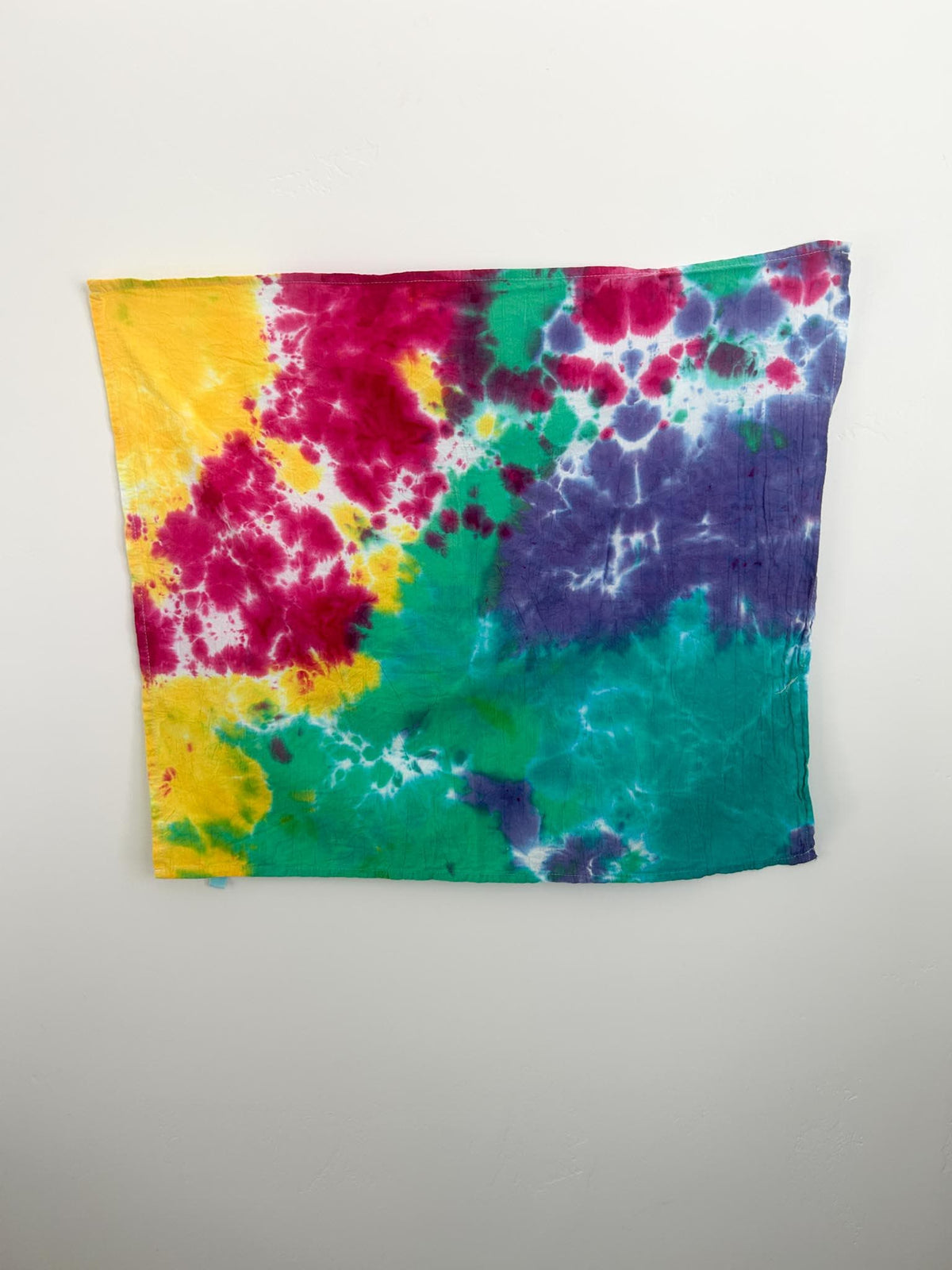 Close up of rainbow tie dye pattern on cotton flour sack towel showing pink, yellow, green, teal, and purple watercolor blends