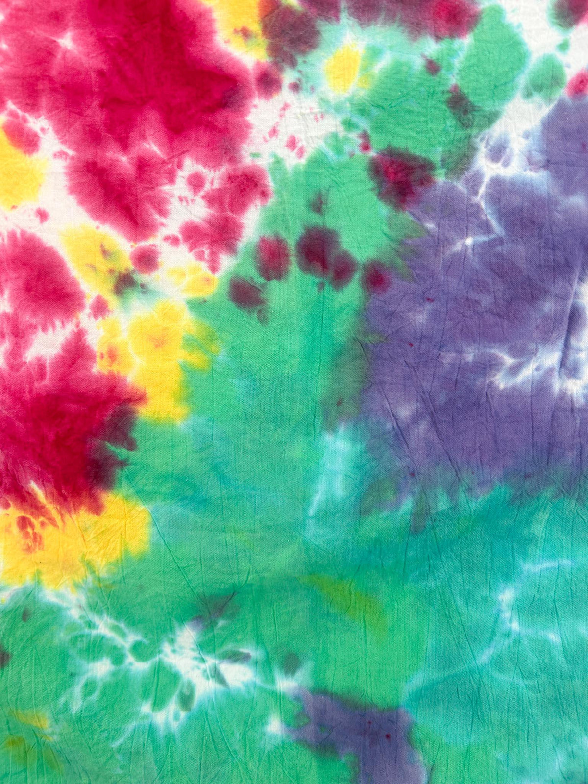 Full view of handmade rainbow tie dye flour sack tea towel hanging flat on white wall, 28 by 28 inches