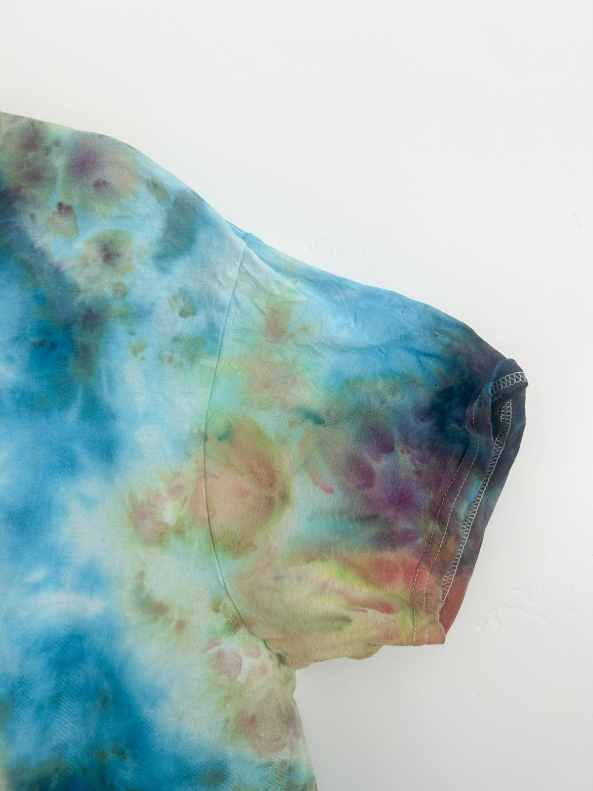 Sleeve and shoulder detail of ice dye t shirt with blue, green, purple, and rust watercolor blooms