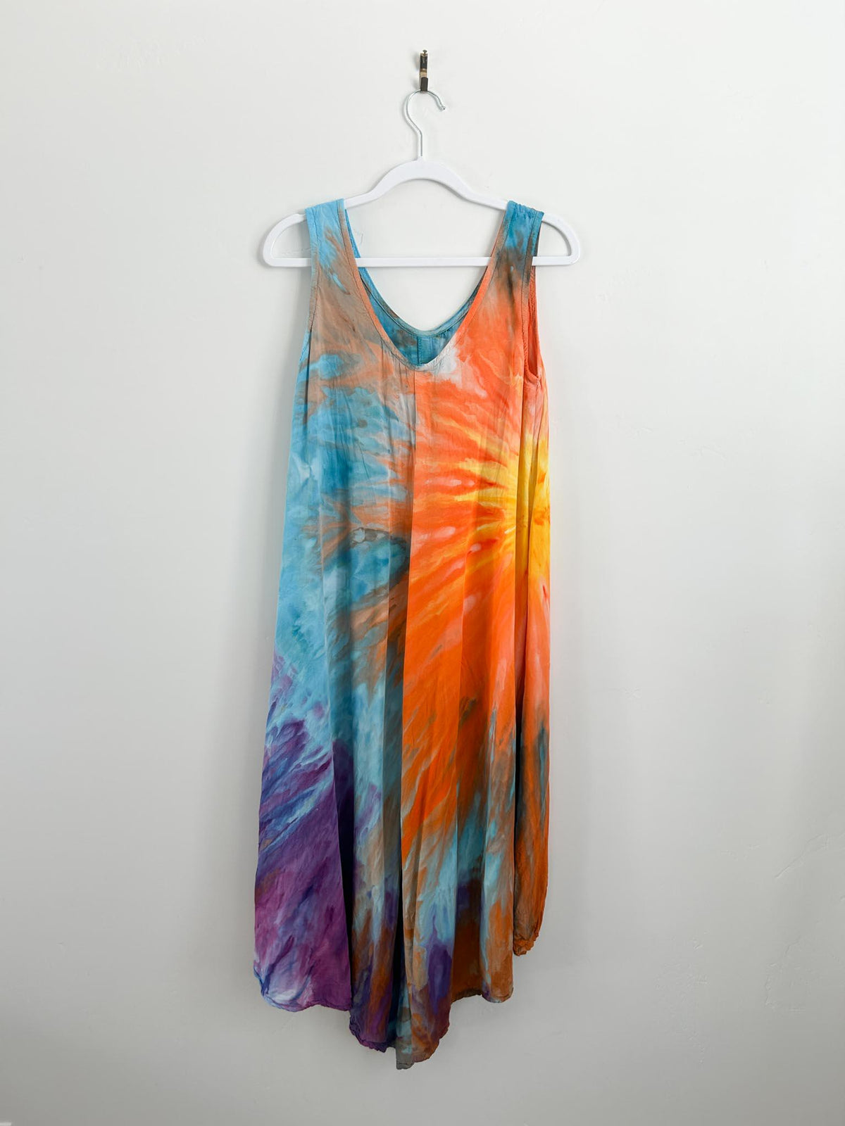 Side angle of handmade tie dye sundress on white hanger with full color story from orange sunburst to blue and purple