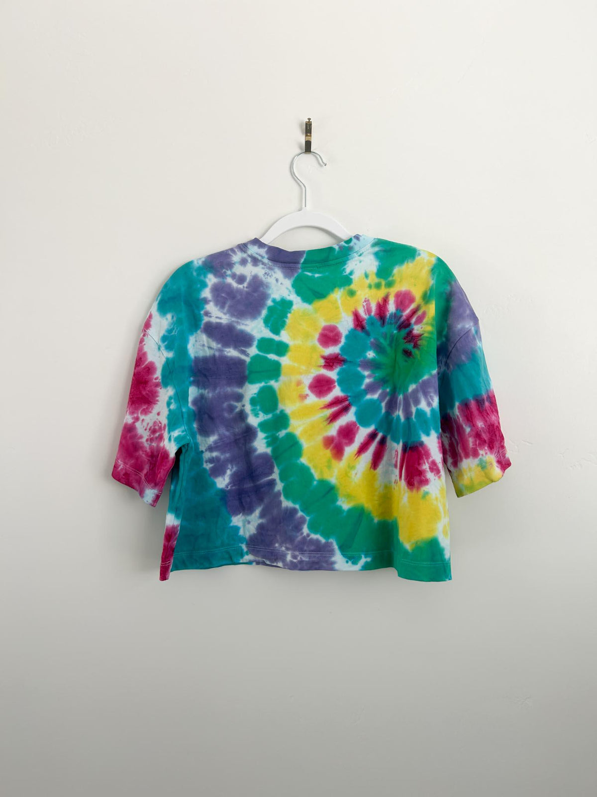 Back of handmade rainbow spiral tie dye crop top in size small on white hanger, pink yellow green teal and purple