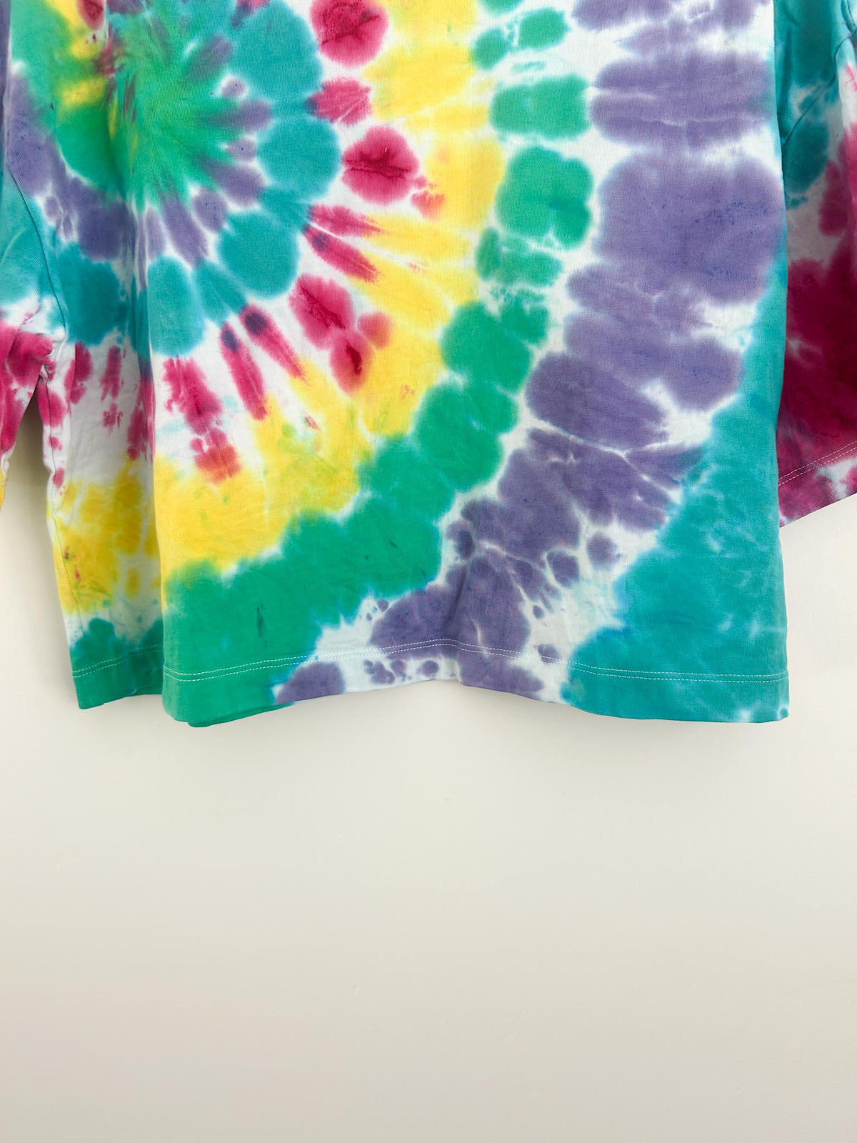 Hem and lower body of rainbow spiral tie dye crop top showing yellow, green, purple, and pink swirl