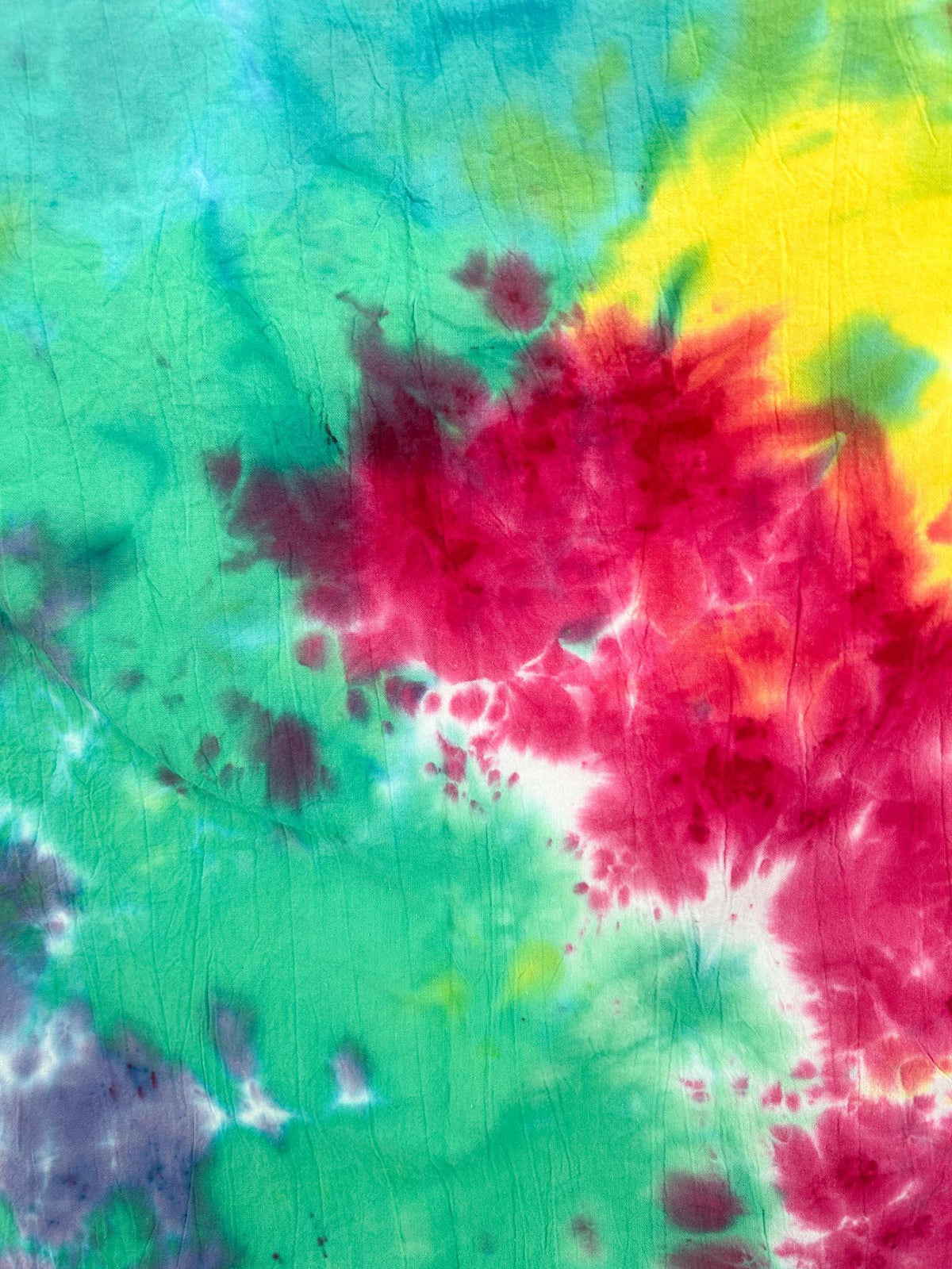 Close up of rainbow tie dye pattern on cotton flour sack towel showing pink, yellow, green, teal, and purple watercolor blends