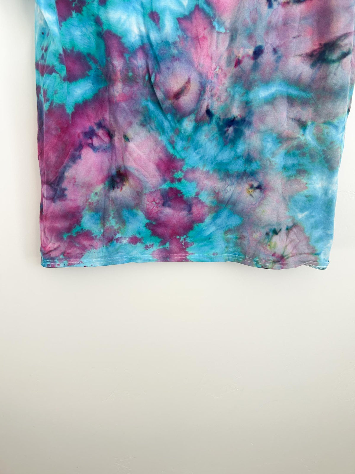 Bottom hem detail of pink and teal ice dye tee with deep magenta and turquoise pattern