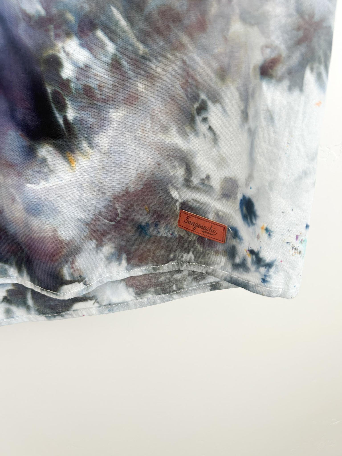 Close-up of a leather brand patch on the hem of a geode ice dye shirt.
