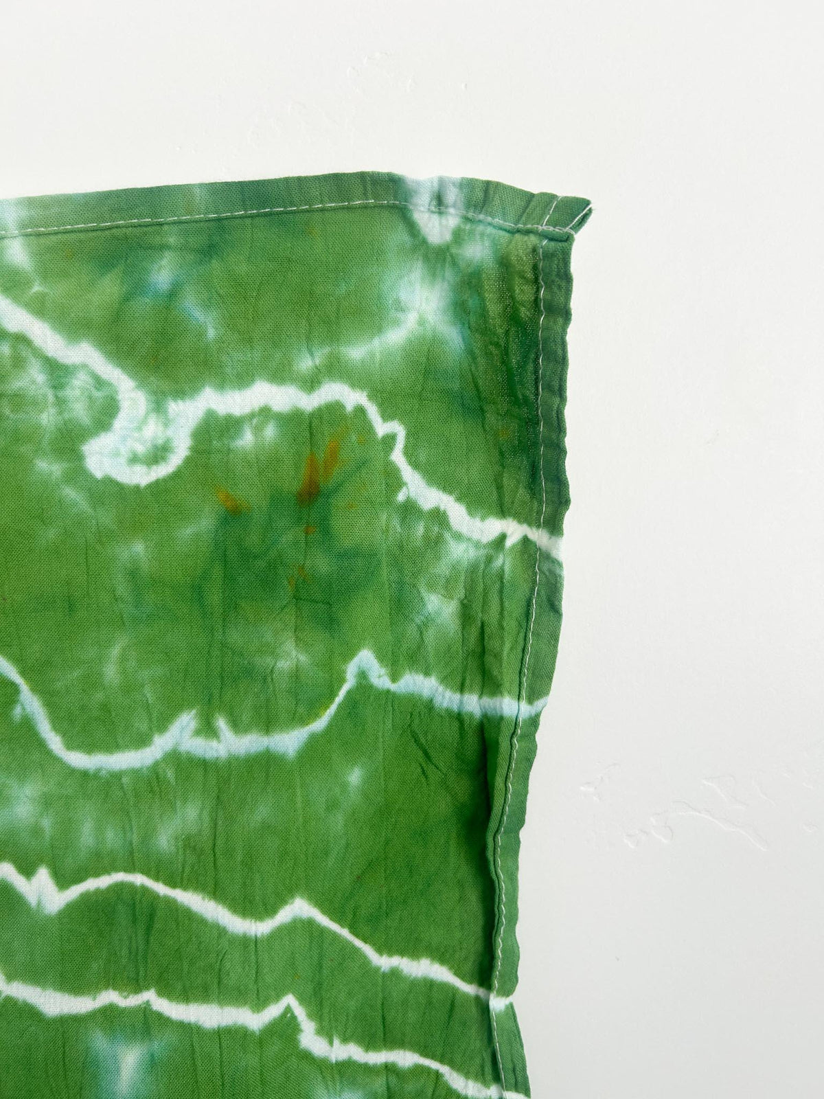 Close-up corner of a green geode tie dye tea towel showing the white hang loop and white geode lines.
