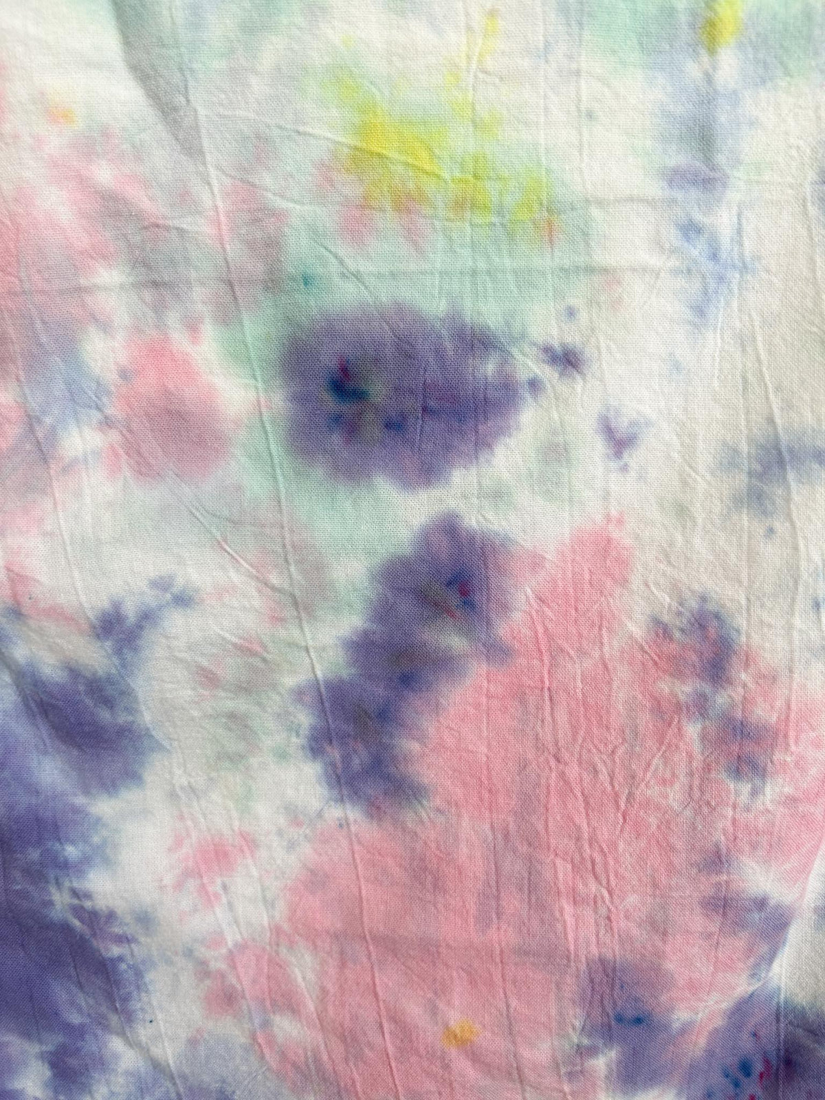 Close-up of a pastel tie dye tea towel showing the scrunch pattern in pink, lavender, and mint.