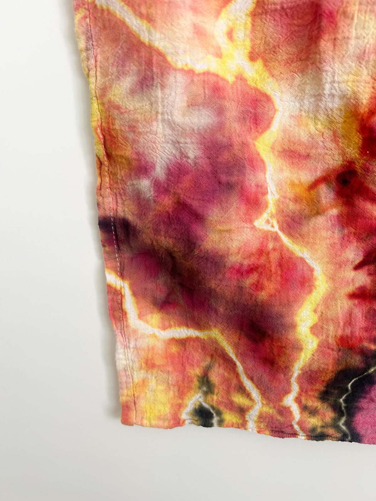Close-up corner of a pink and orange ice dye tea towel showing the crackled white geode lines and hemmed edge.