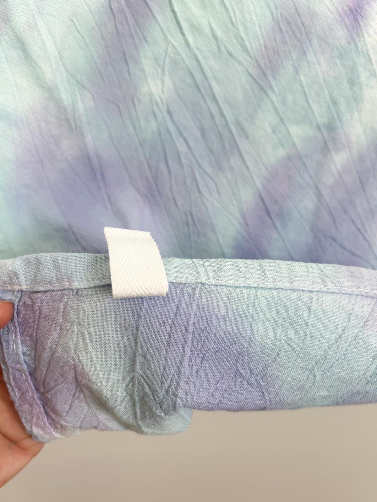 Close-up of the hem and hang loop on a mint and lavender liquid dye tea towel, showing the rolled dye lines.