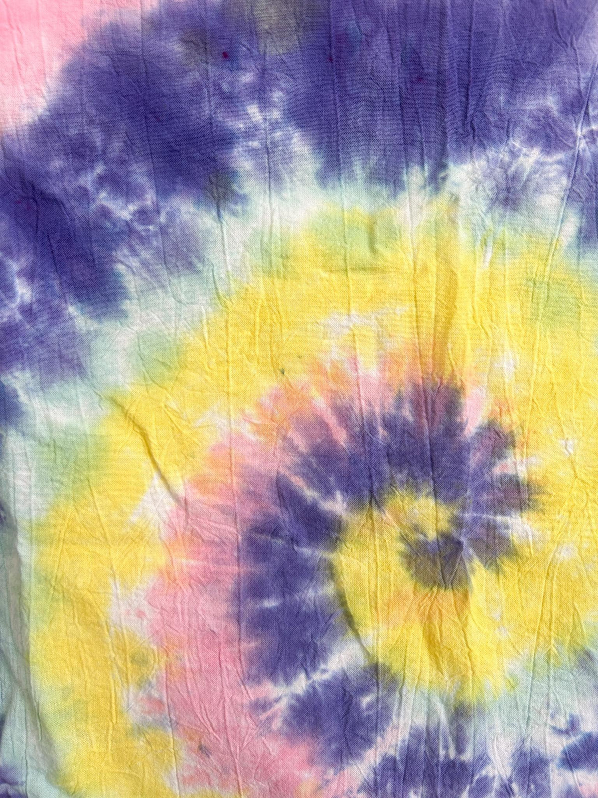 Close-up of the spiral center on a pastel tie dye tea towel in purple, yellow, and pink.