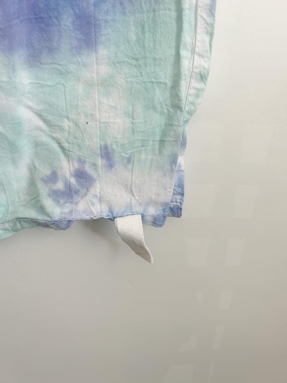 Close-up corner of a blue and mint pastel liquid dye tea towel showing the white hang loop and soft color blending.