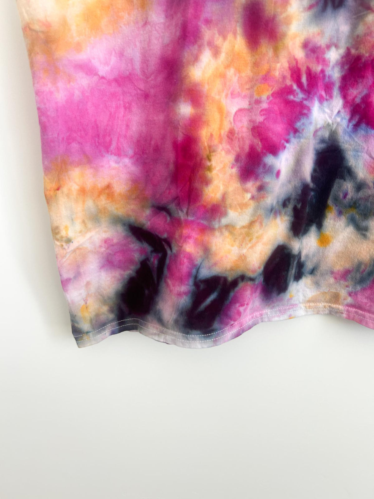 Close-up of the hem on a pink, orange, and charcoal ice dye t-shirt.