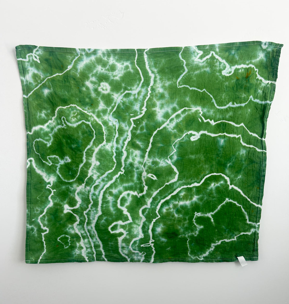 Green and white geode tie dye cotton tea towel hanging flat, with white ring patterns on a green background.