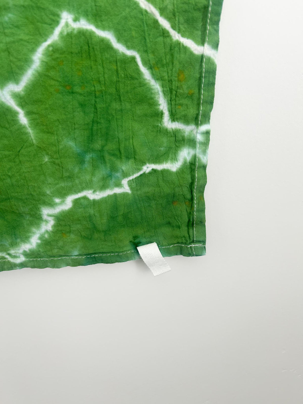 Close-up corner of a green hand dyed tea towel showing the geode ring pattern and hemmed edge.