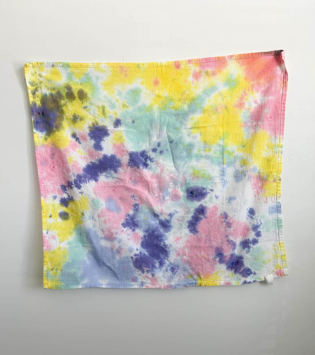 Multicolor pastel tie dye cotton tea towel hanging flat, with soft pink, yellow, lavender, and mint on a white base.