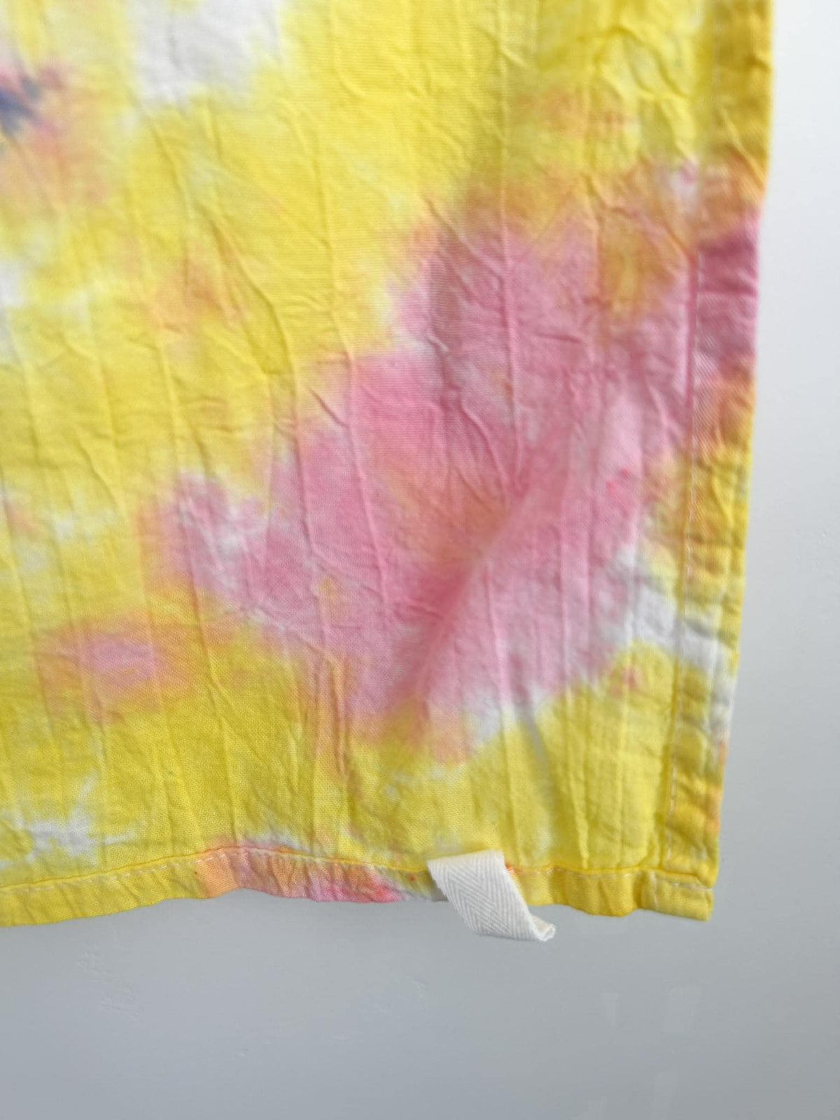 Close-up corner of a pink and yellow heart tie dye tea towel showing the white hang loop.