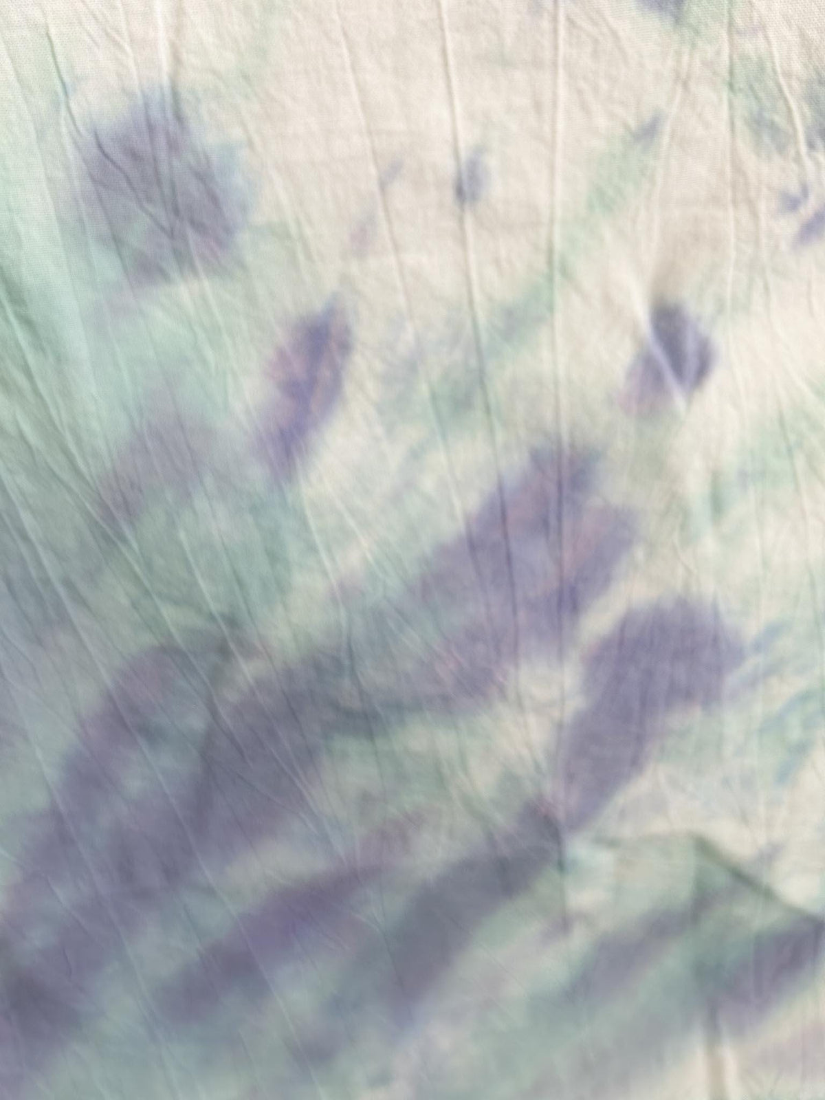 Close-up of a pastel tie dye tea towel showing soft lavender and mint blending into white.