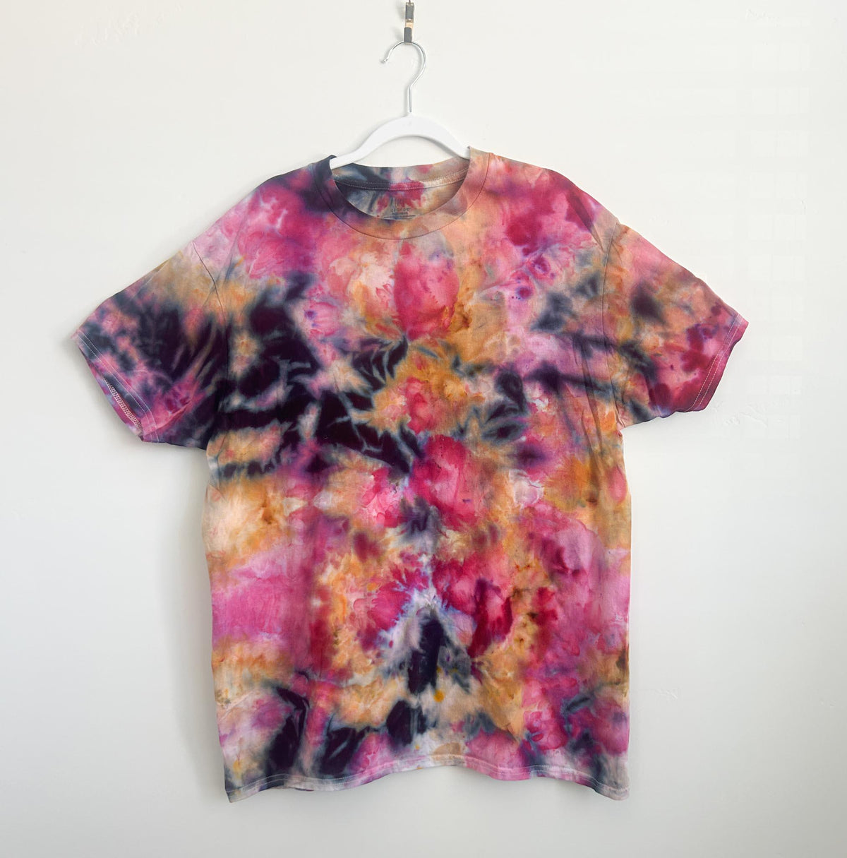 Front of an ice dye cotton t-shirt in hot pink, fuchsia, orange, and charcoal on a hanger.
