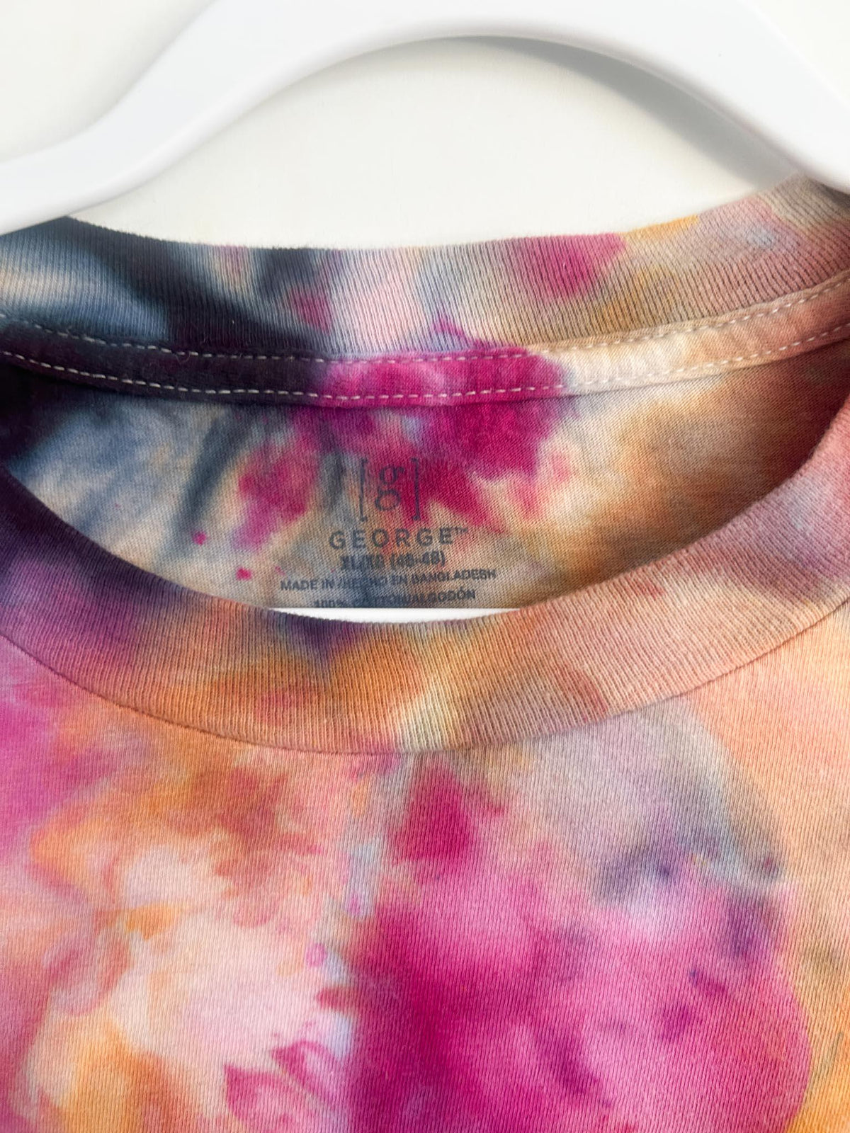 Close-up of the crew neck and label on a pink and orange ice dye t-shirt showing George XL cotton.
