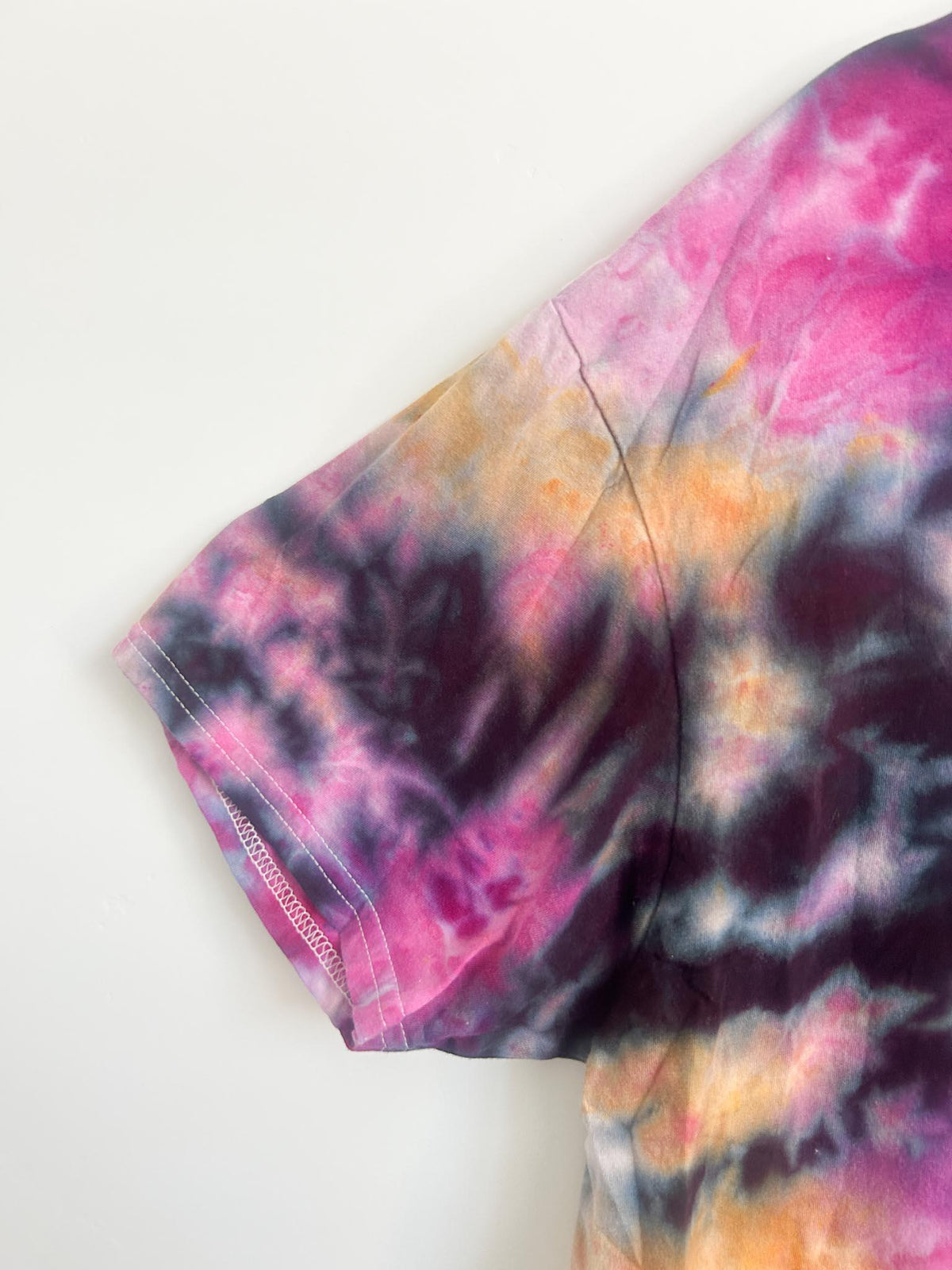Close-up of the sleeve on a pink, orange, and black ice dye cotton t-shirt.