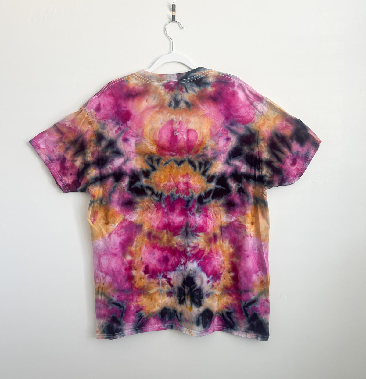 Back of an ice dye cotton t-shirt showing a mirrored kaleidoscope pattern in hot pink, orange, and charcoal.