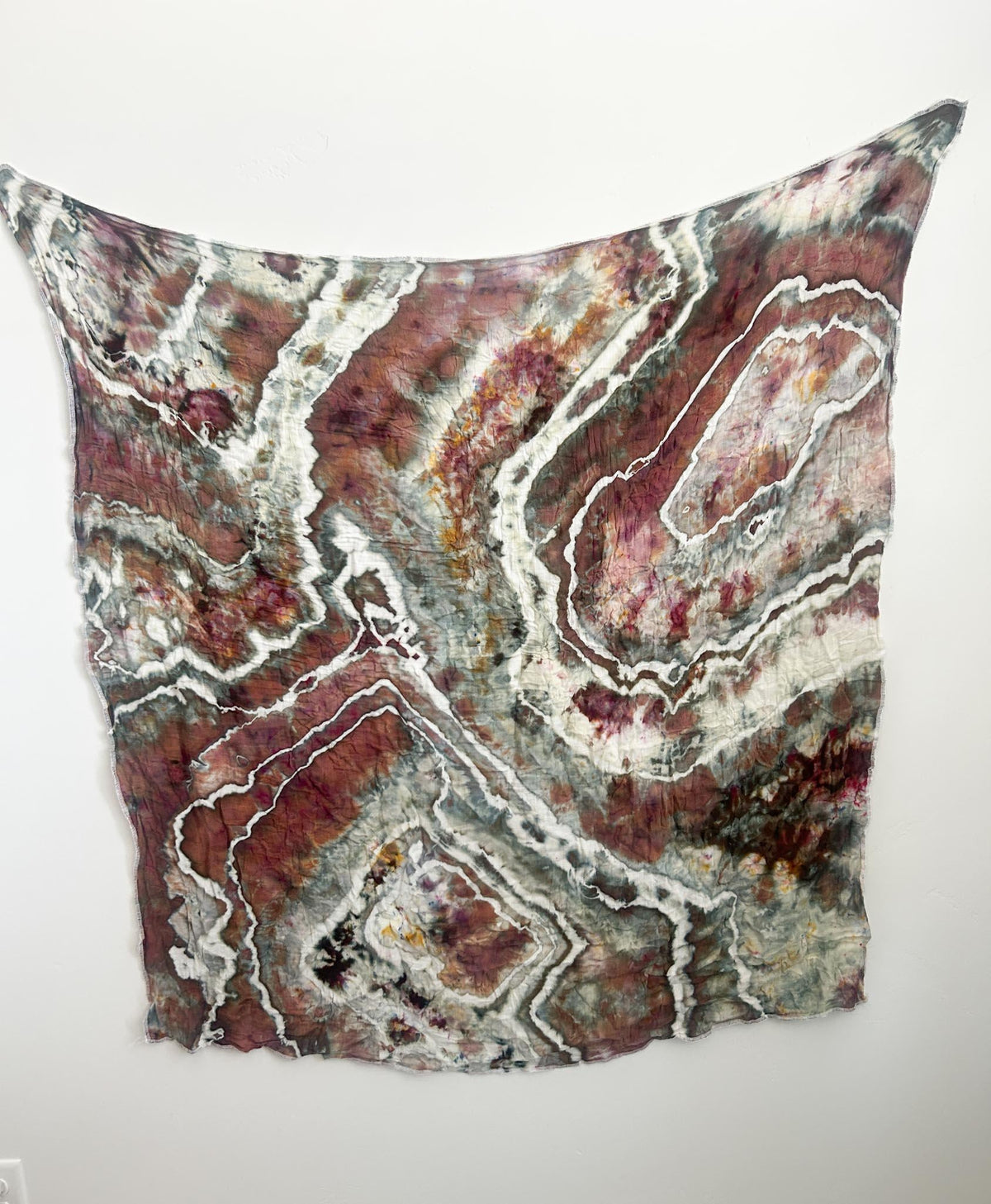 Hand dyed ice dye swaddle blanket in earthy sage, mauve, and rust with white geode rings, hanging flat.