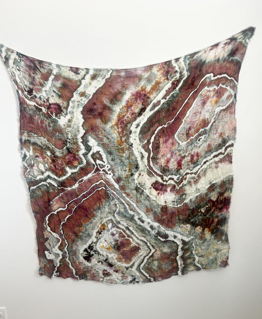 Hand dyed ice dye swaddle blanket in earthy sage, mauve, and rust with white geode rings, hanging flat.