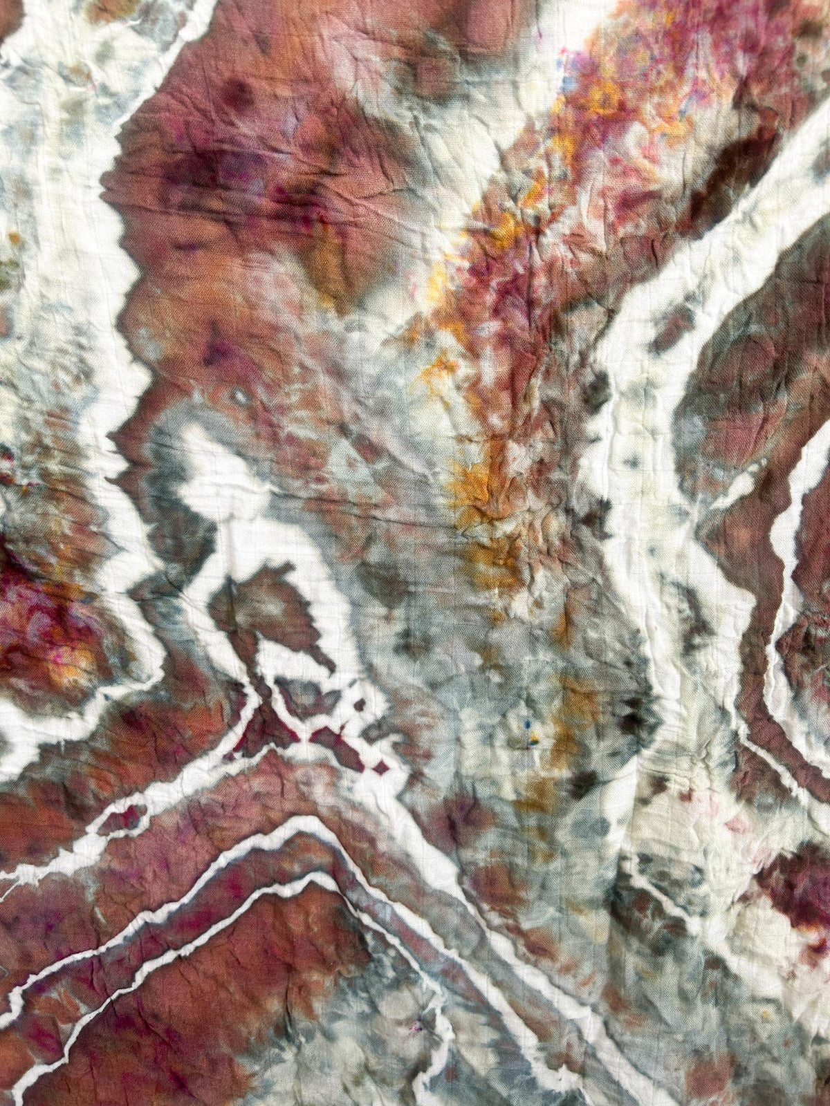 Close-up of the geode ice dye pattern on a muslin swaddle in earthy sage, mauve, and gold tones.