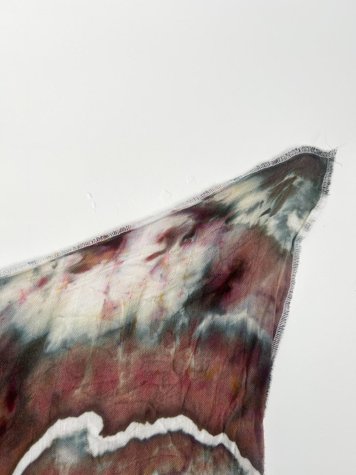 Close-up corner of an ice dye swaddle blanket showing the serged edge and earthy geode colors.