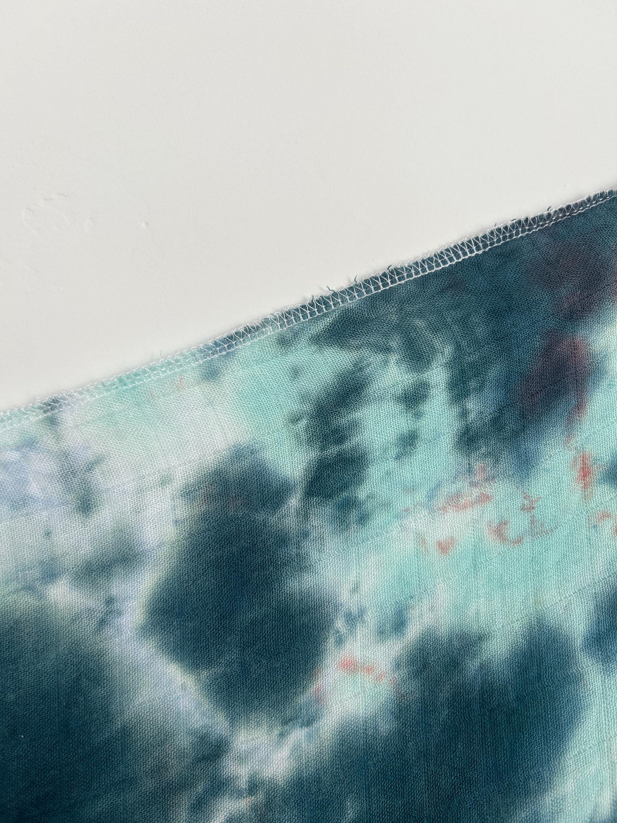 Close-up corner of a coral and charcoal liquid dye bamboo swaddle showing the serged edge.