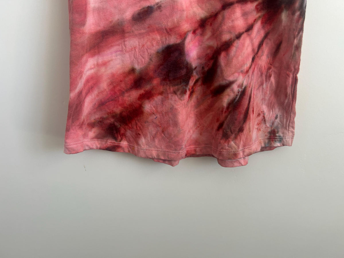 Close-up of the lower hem of a hand dyed tank, showing deep oxblood and maroon ice dye bleeding through a dusty pink base.
