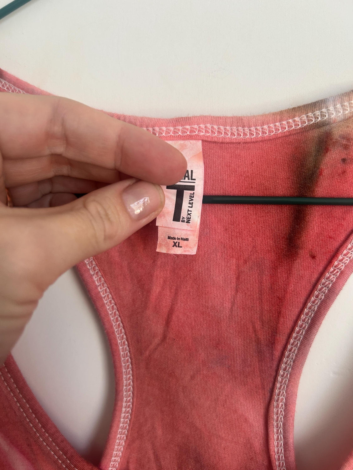 Close-up of the neckline on a hand dyed coral and maroon ice dye racerback tank, showing the Next Level size XL tag and white stitching.
