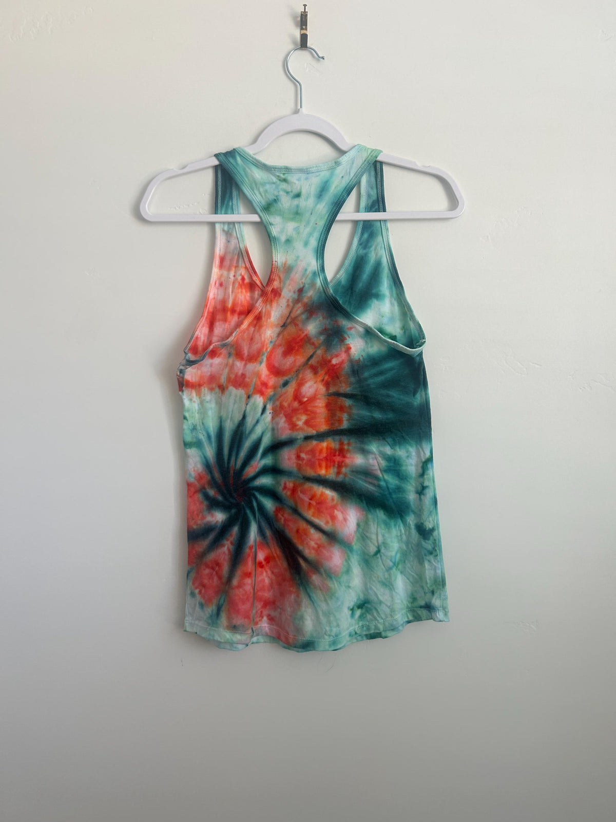 Back view of a teal and red spiral ice dye racerback tank on a hanger, showing sea-green coloring and a coral-orange swirl.